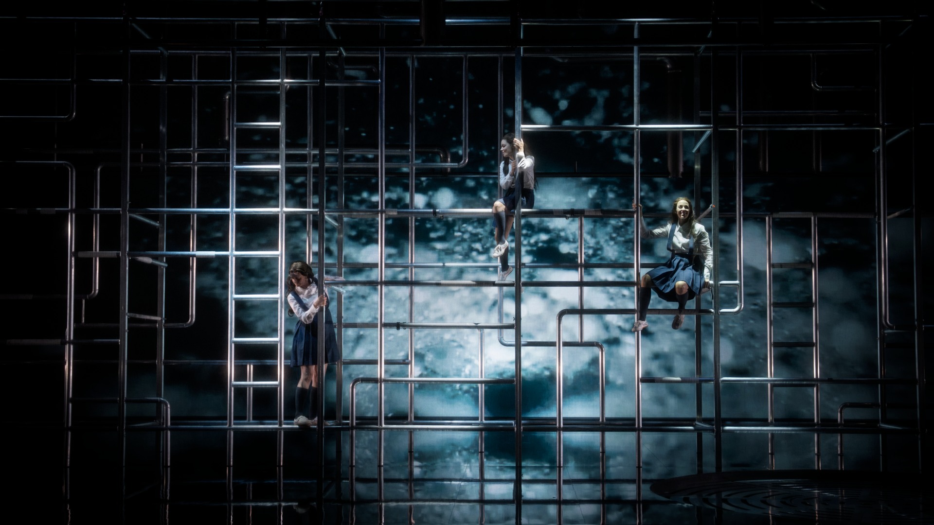 Mot en vattenfond syns en mängd rör: i rören klättrar tre kvinnor.