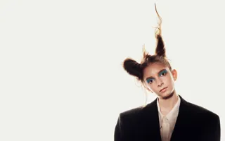 En ung kvinna, iförd mörk kavaj och med håret uppsatt i två koner, huvudet lätt lutat åt sidan, mot en vit bakgrund.