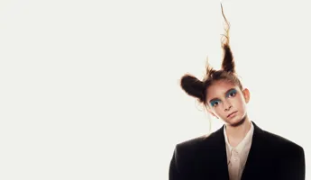 En ung kvinna, iförd mörk kavaj och med håret uppsatt i två koner, huvudet lätt lutat åt sidan, mot en vit bakgrund.