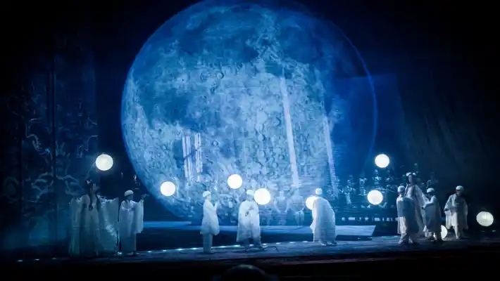 En scenbild med flera personer som rör sig i ett blåtonat landskap, i bakgrunden syns en stor himlakropp.