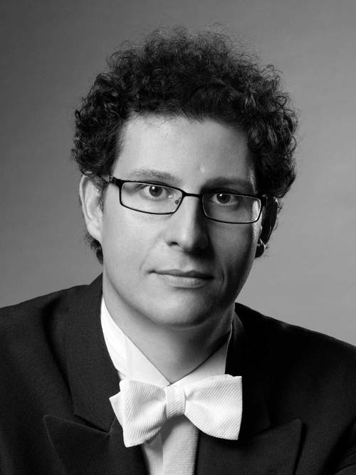 En närbild på en man med lockigt hår, han bär glasögon och bär frack.