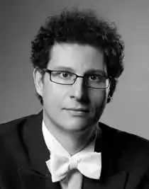 En närbild på en man med lockigt hår, han bär glasögon och bär frack.