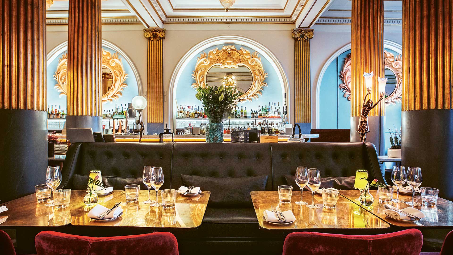 En interiör med dukade bord och en bar i bakgrunden, rikt utsmyckad med guldpelare.