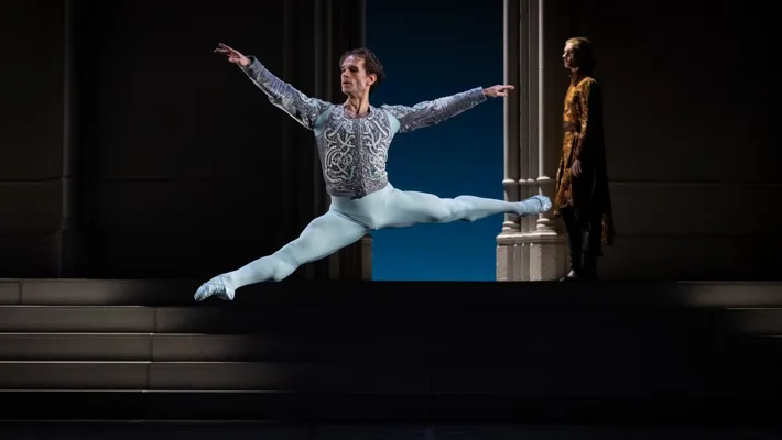 A male dancer does a big, high jump on a stage.