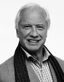 Porträttbild på en man med ljust hår, klädd i kavaj och med en draperad halsduk.
