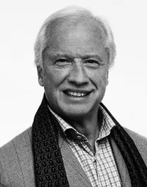 Portrait image of a man with blond hair, wearing a jacket and a draped scarf.