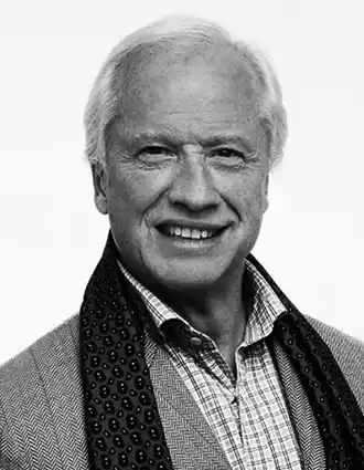 Porträttbild på en man med ljust hår, klädd i kavaj och med en draperad halsduk.