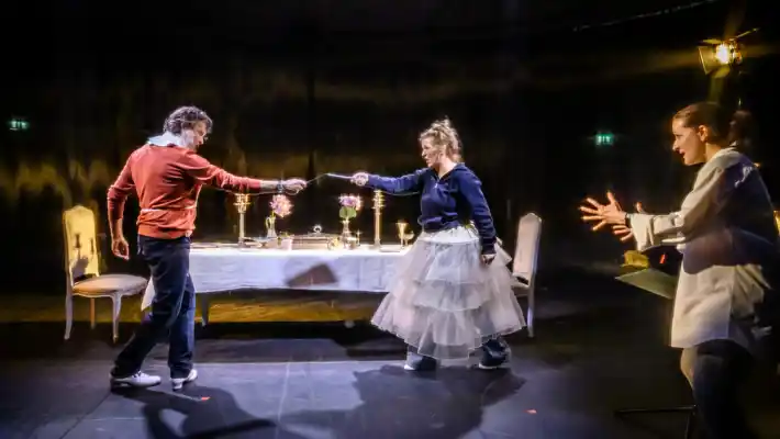 En kvinna och en man pekar mot varandra, vid sidan av dem ytterligare en kvinna som verkar ge dem instruktioner.