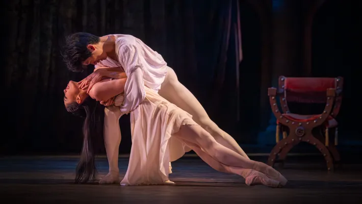 Två dansare, en man och en kvinna, i en öm rörelse där han håller henne i sina armar.