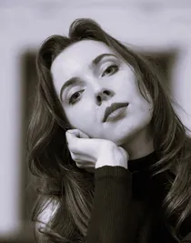 En närbild på en kvinna med långt mörkt hår, hon lutar huvudet mot vänster och vilar det i sin hand.