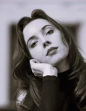 En närbild på en kvinna med långt mörkt hår, hon lutar huvudet mot vänster och vilar det i sin hand.