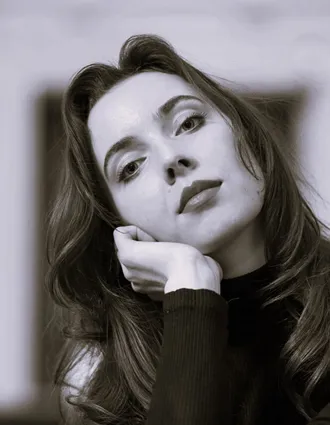 En närbild på en kvinna med långt mörkt hår, hon lutar huvudet mot vänster och vilar det i sin hand.