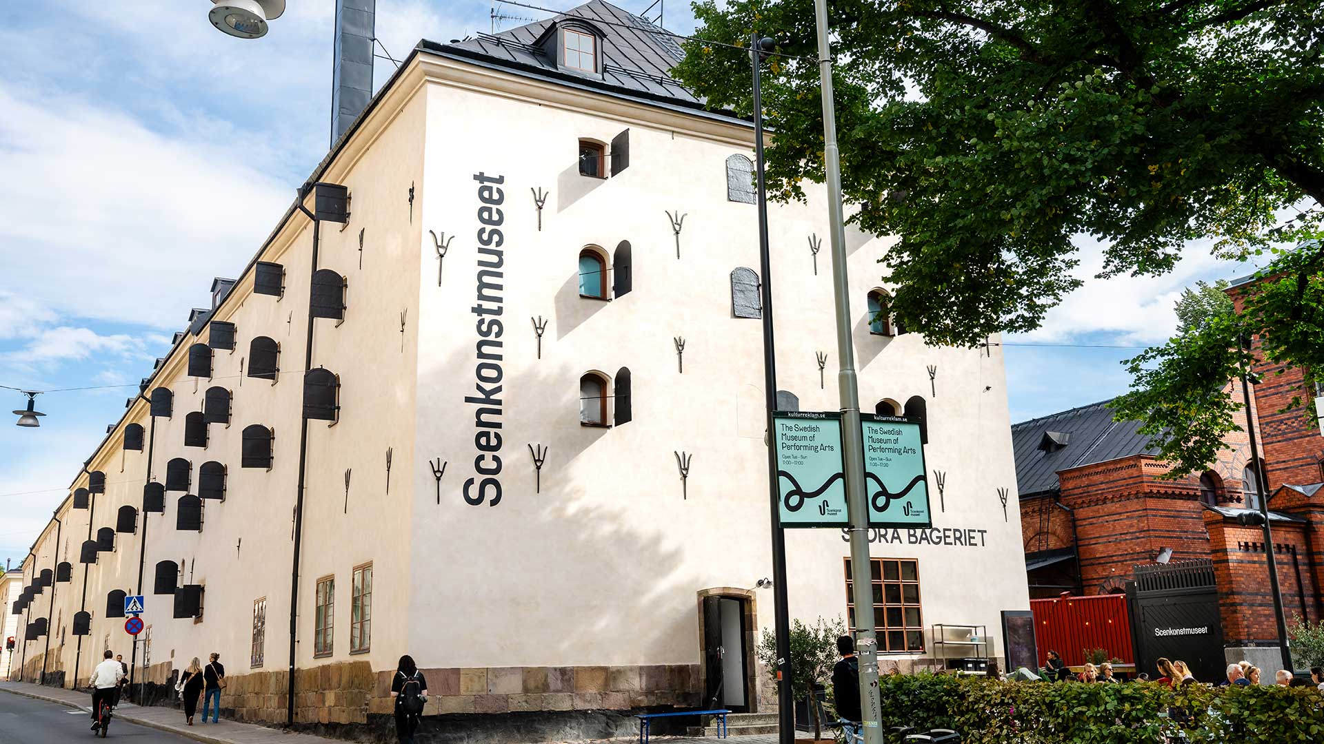 En vit byggnad med många fönsterluckor och stort träd framför.