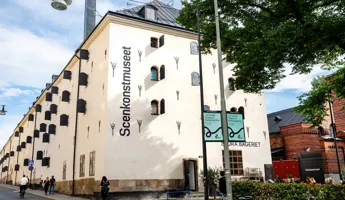 En vit byggnad med många fönsterluckor och stort träd framför.