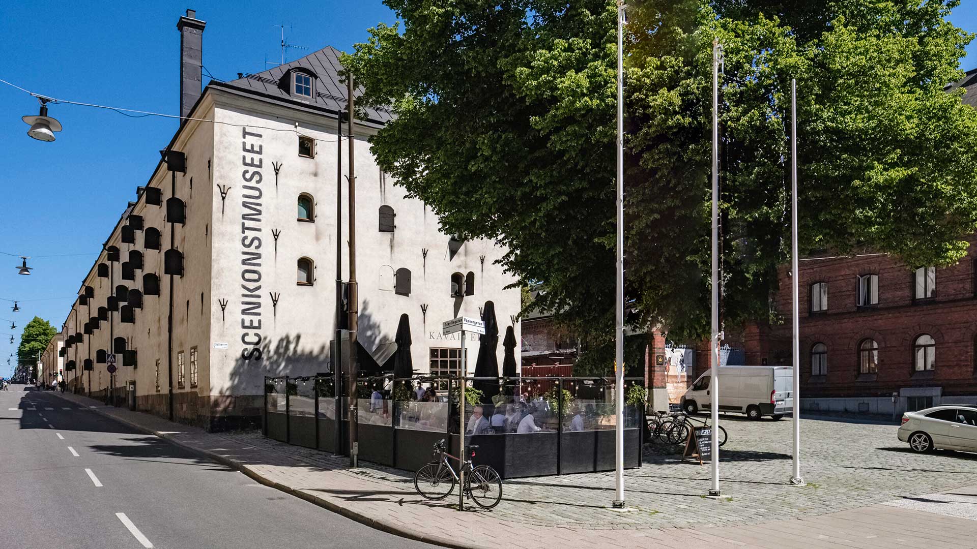 En vit byggnad med många fönsterluckor och stort träd framför.