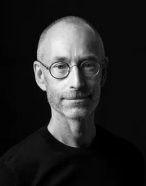 Närbild på en snaggad man med skägg och glasögon.