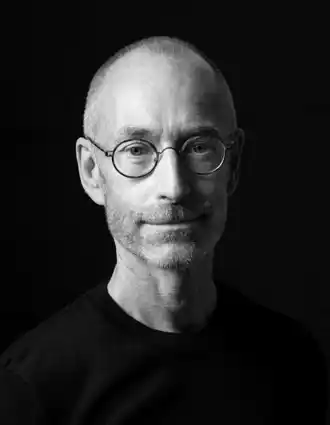 Närbild på en snaggad man med skägg och glasögon.