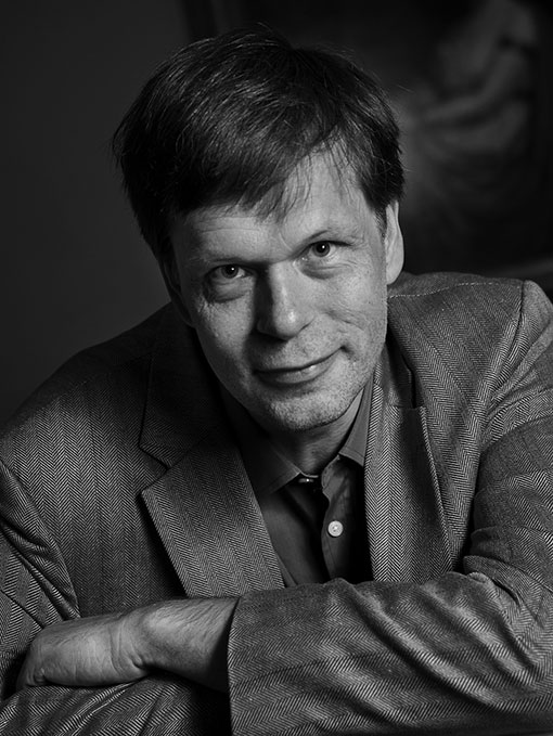 A close-up of a smiling man, leaning slightly forward, wearing a suit.