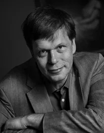 A close-up of a smiling man, leaning slightly forward, wearing a suit.
