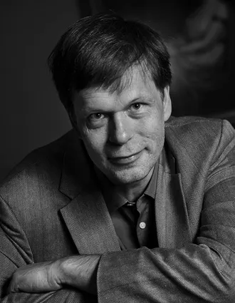 En närbild på en leende man, lätt framåtlutad, klädd i kostym.