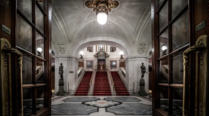 View of a large entrance hall, a staircase with red carpet leads up to a door.