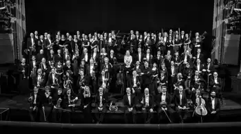 Ett hundratal uppklädda personer står på en scen, flera har med sig instrument.