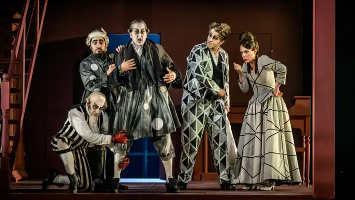 Several figures in graphic clothing stand on a stage surrounded by decor depicting a house.