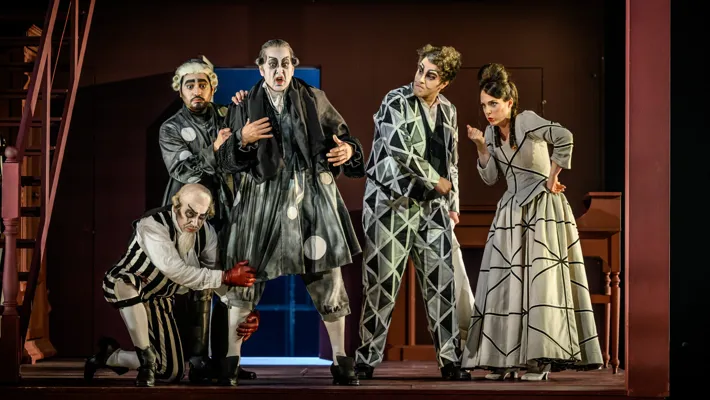 Several figures in graphic clothing stand on a stage surrounded by decor depicting a house.