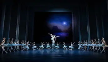 A moon shines over a stage with dancers in formation; in the center, a male dancer lifts a female dancer.