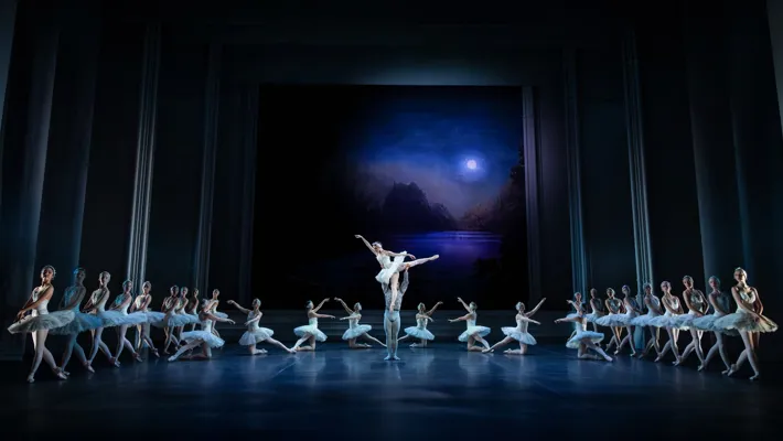 A moon shines over a stage with dancers in formation; in the center, a male dancer lifts a female dancer.
