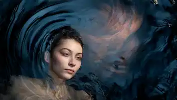 A dark-haired woman looks at us, she is half submerged in dark water.