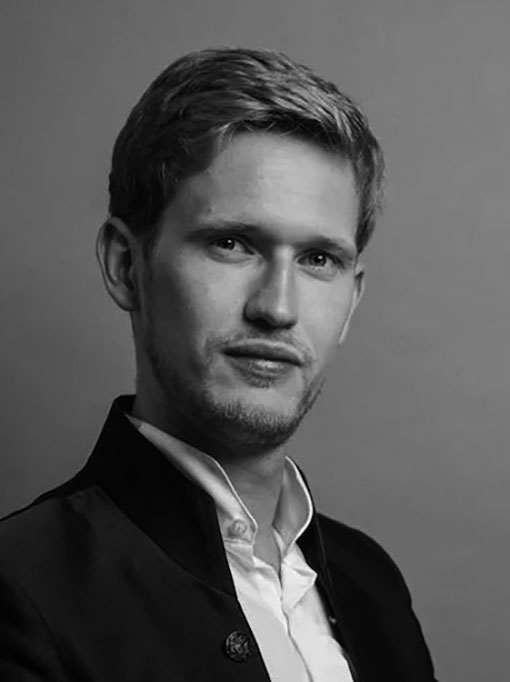 A close-up of a fair-haired man with a white shirt and dark jacket.