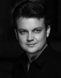 En närbild på en ung man iklädd mörk skjorta, han blickar ut mot höger.