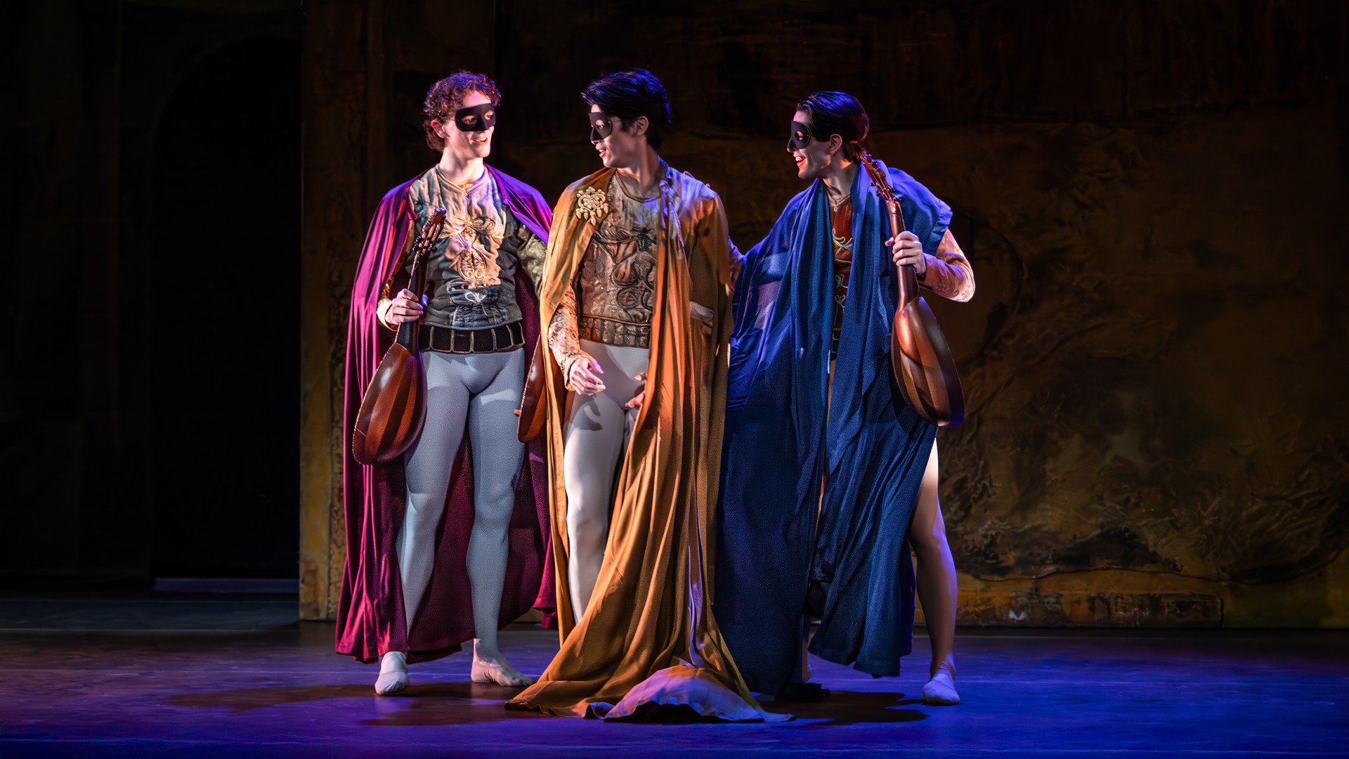 Tre män med masker och långa mantlar, två håller i lutor; de verkar samtala med varandra.