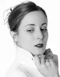 Närbild på en kvinna i vit skjorta, kragen är uppvikt och hon håller i den med båda händerna.