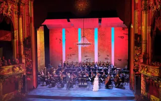 En vackert upplyst scen, omgärdad av gulddekor, med orkester och sångare i förgrunden.