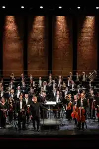 Many musicians stand spread out on a large stage.