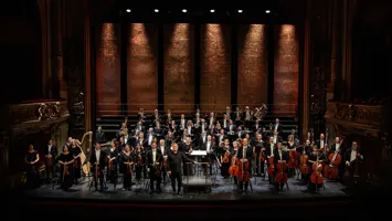 Many musicians stand spread out on a large stage.