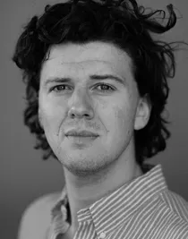 Närbild på en man med yvigt hår och en randig skjorta.