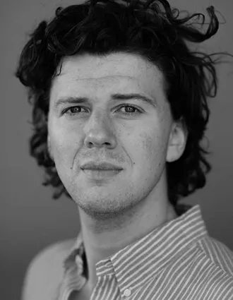 Närbild på en man med yvigt hår och en randig skjorta.