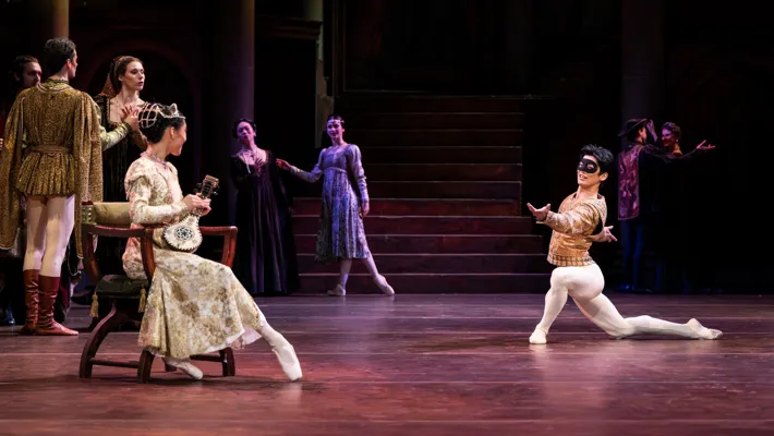 Flera dansare på en scen, en man knäböjer inför en kvinna sittandes i en stol.