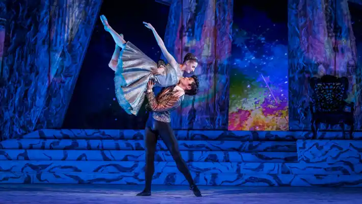 A male dancer lifts a female dancer high.
