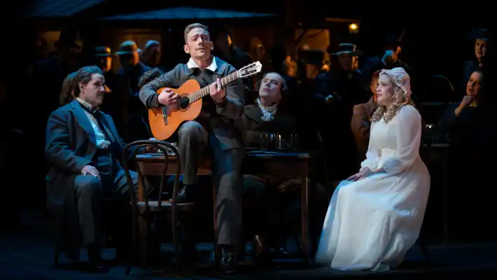 En grupp människor som sitter runt ett bord med en man som spelar gitarr.