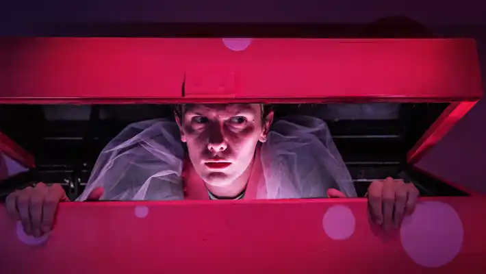 En pojke med ett en något lömsk blick tittar ut från en leksakslåda.