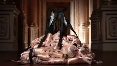 Two black pointe shoes stand at the top of a pile of pink pointe shoes.