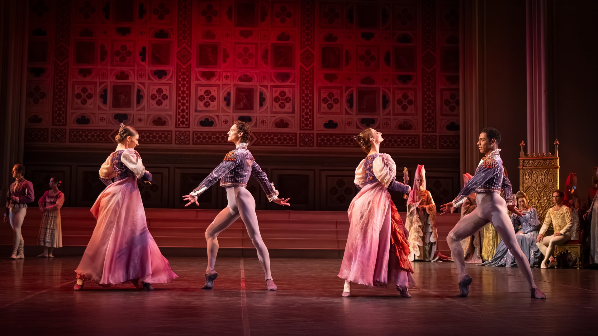 Two couples dance on a stage while several people watch.