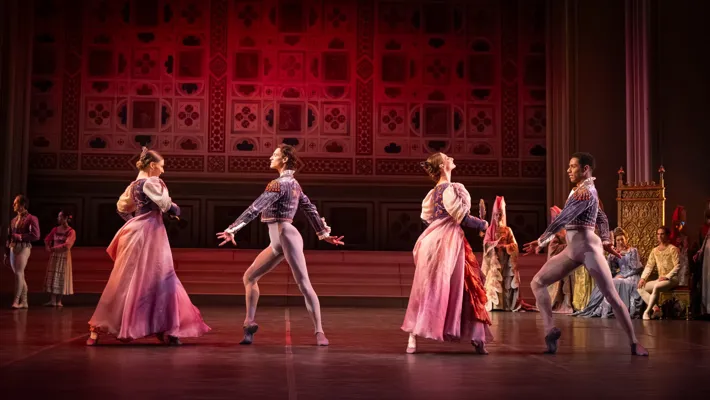 Two couples dance on a stage while several people watch.