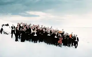 En samling personer i svarta kostymer, några med instrument, står i ett vinterslandskap.