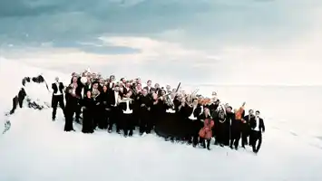 A group of people in black suits, some with instruments, stand in a winter landscape.