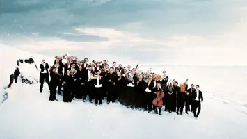 En samling personer i svarta kostymer, några med instrument, står i ett vinterslandskap.